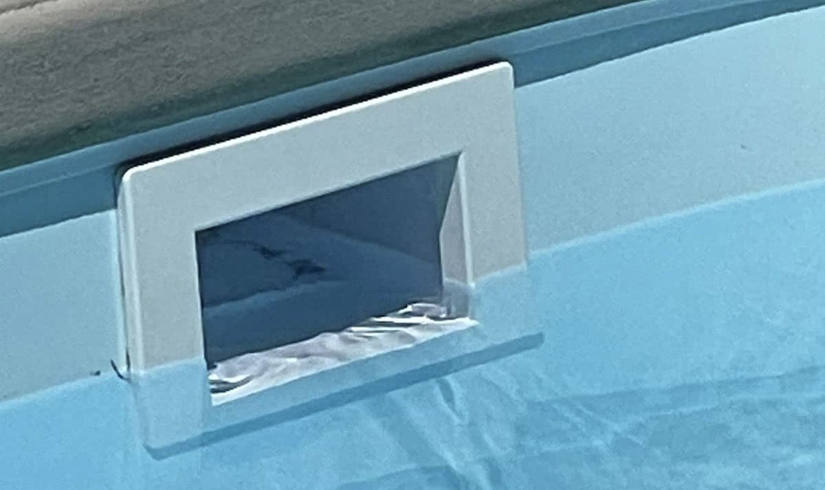 Close-up of a swimming pool skimmer with a rectangular opening on the pool wall, captured during routine pool services in Suffolk County NY. The water ripples gently towards the skimmer, while part of the pool's edge is visible at the top.